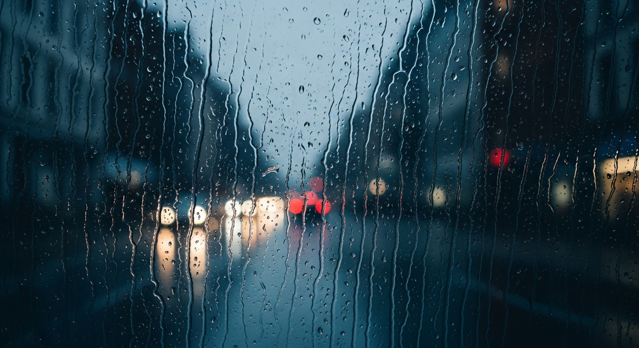 Blurred street scene with cars and pedestrians, viewed through a rain-streaked window.